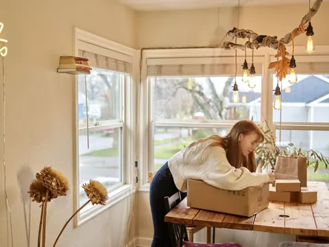 Una emprendedora sella una caja de pedido junto a la ventana
