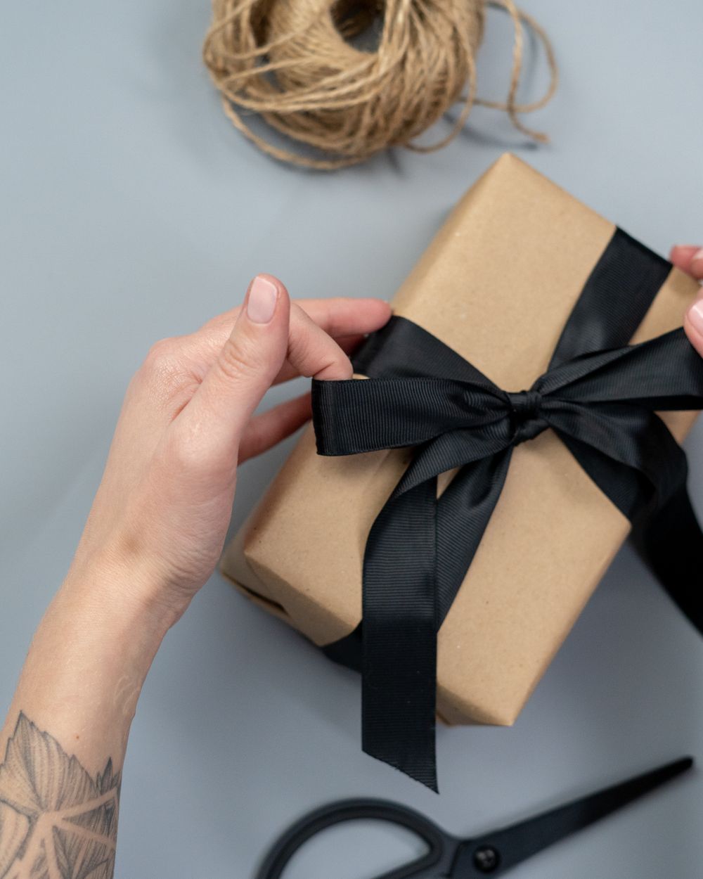 Unas manos atan un moño negro a un regalo envuelto en papel kraft